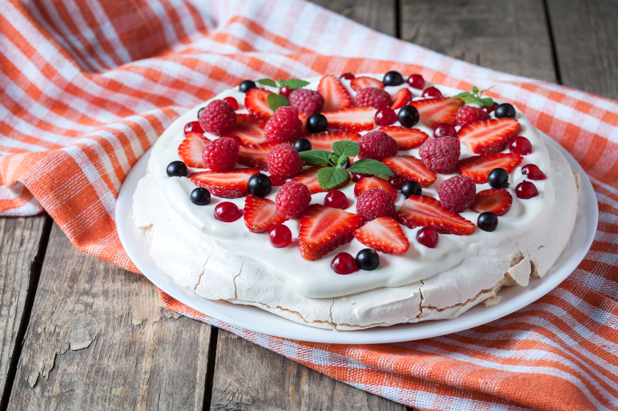 Organic homemade traditional meringue dessert sweet cake with whipper cream, strawberry, blackberry and mint on white plate. Vintage wooden background table. Rustic style and natural light.